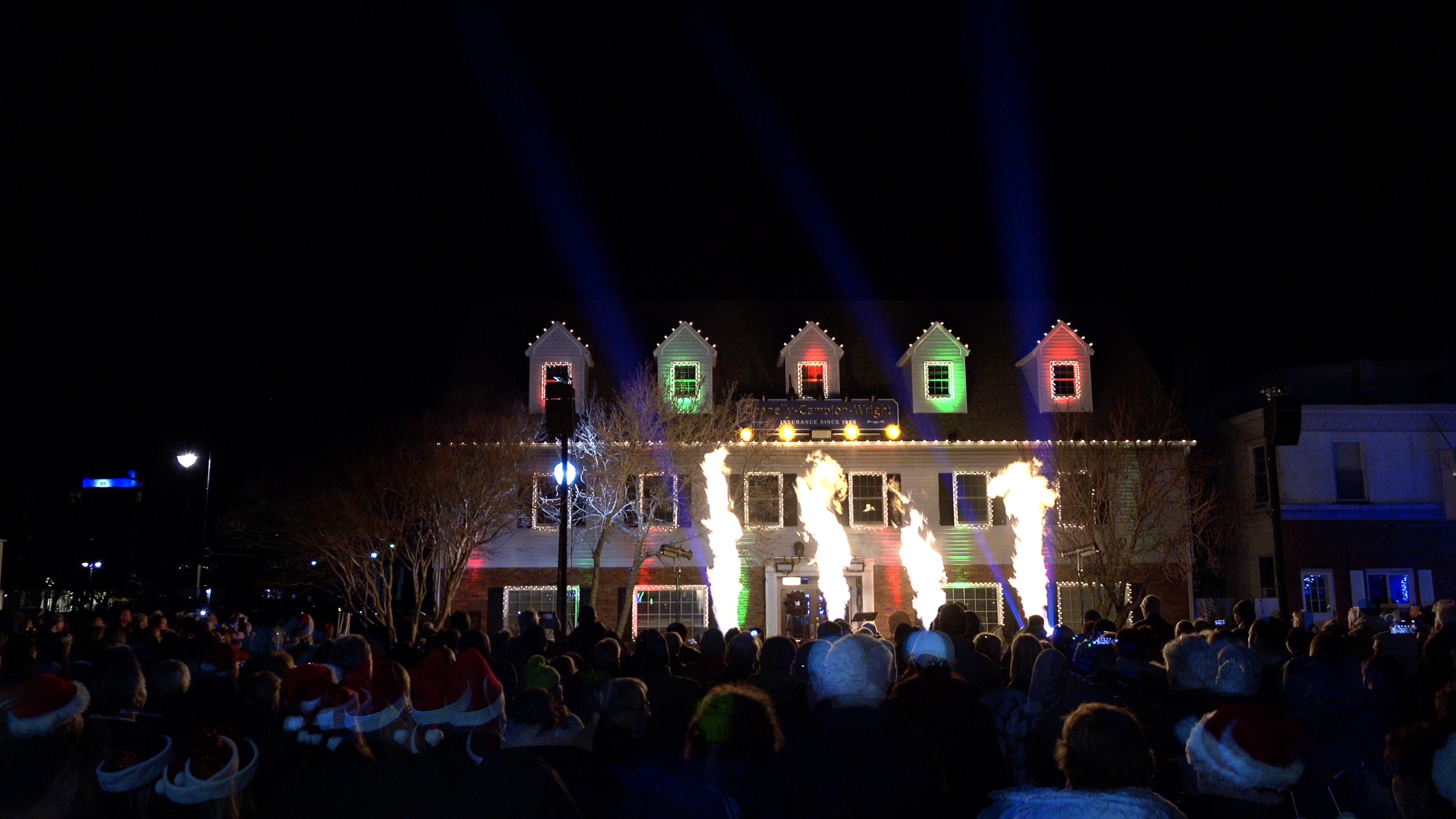 Flames and red and green lights on the Connelly-Campion-Wright building as the crowd watches at Belmar Plaza